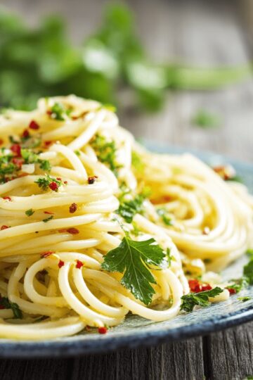 Spaghetti Aglio e Olio auf einem blauen Keramik Teller, der auf einem Holztisch steht